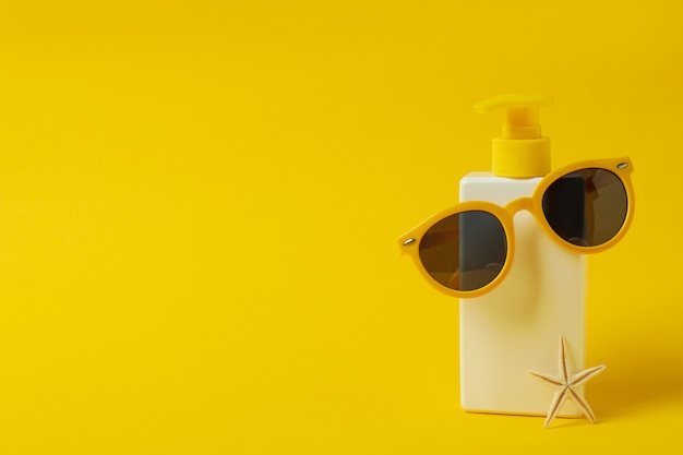 Bottiglia di crema solare con occhiali da sole e stelle marine su sfondo giallo isolato