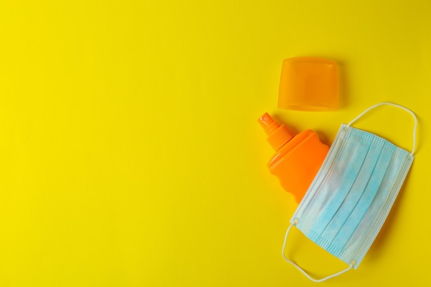 Bottiglia di crema solare e mascherina medica su colore giallo