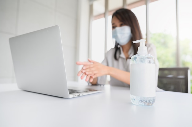 Bottiglia di gel di alcol con una donna che indossa la maschera facciale lavando la mano