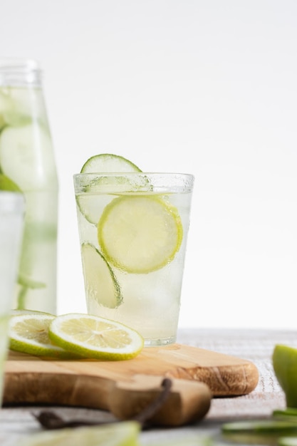 Bottiglia di limonata e un bicchiere servito con fette di limone e cetriolo su sfondo chiaro Copia spazio