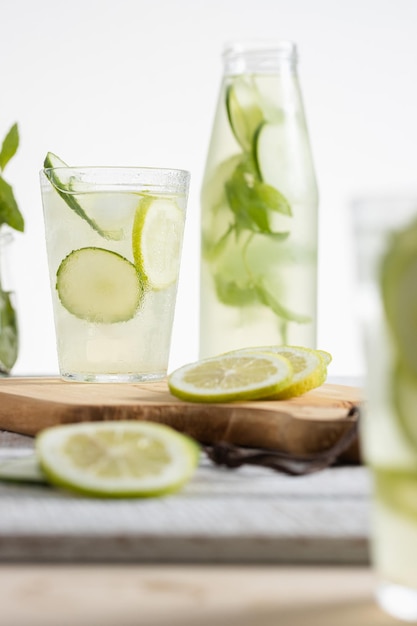 Bottiglia di limonata e un bicchiere servito con fette di limone e cetriolo su sfondo chiaro Copia spazio