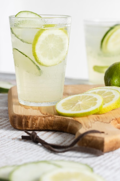 Bottiglia di limonata e un bicchiere servito con fette di limone e cetriolo su sfondo chiaro Copia spazio