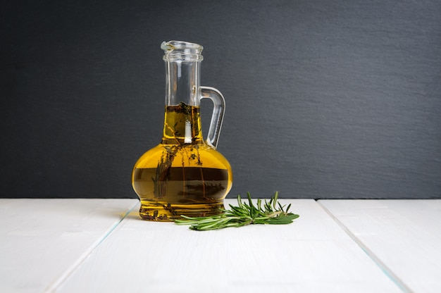 Bottiglia di olio d'oliva, ramo di rosmarino fresco sul tavolo di legno bianco