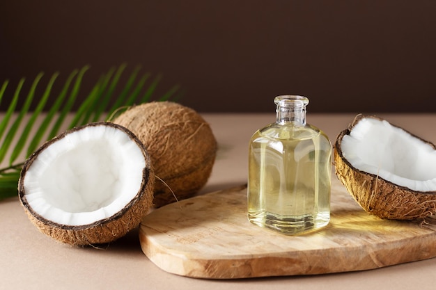 Bottiglia di olio di cocco e noci di cocco fresche con foglia di palma su tavola di legno su sfondo marrone