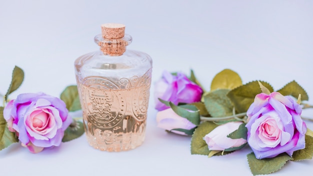 Bottiglia di olio essenziale e fiori finti su superficie bianca