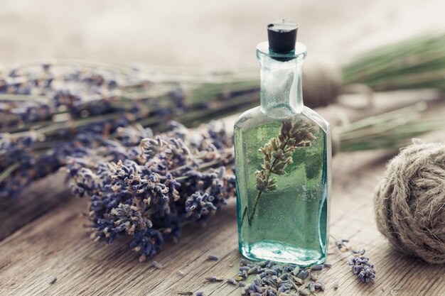 Bottiglia di olio essenziale e mazzo di fiori di lavanda sul tavolo Foto dai toni retrò