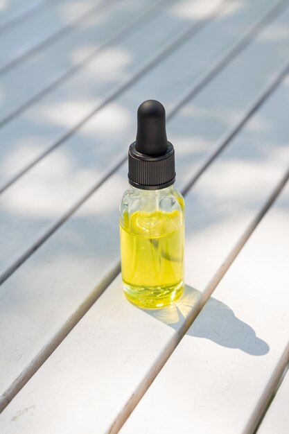 Bottiglia di olio essenziale in vetro bianco con pipetta su fondo di legno con ombre dure Concetto di cura della pelle con cosmetici naturali