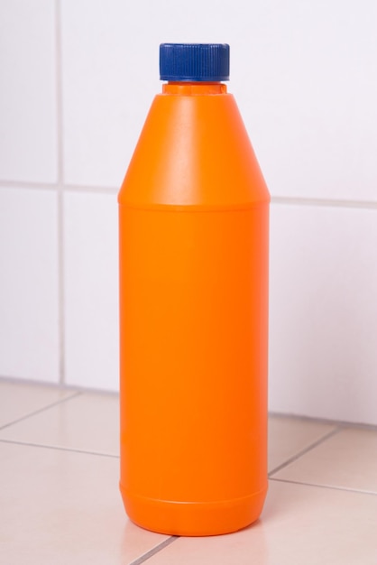 Bottiglia di plastica arancione di prodotto per la pulizia sul pavimento piastrellato