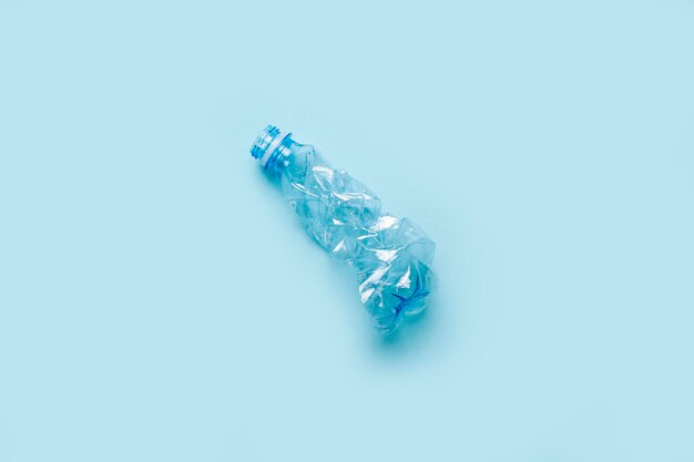 Bottiglia di plastica stropicciata usata su sfondo azzurro Vista dall'alto piatto
