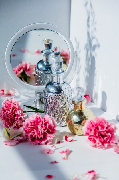 Bottiglia di profumo con specchio e fiori di dianthus intorno sul muro bianco