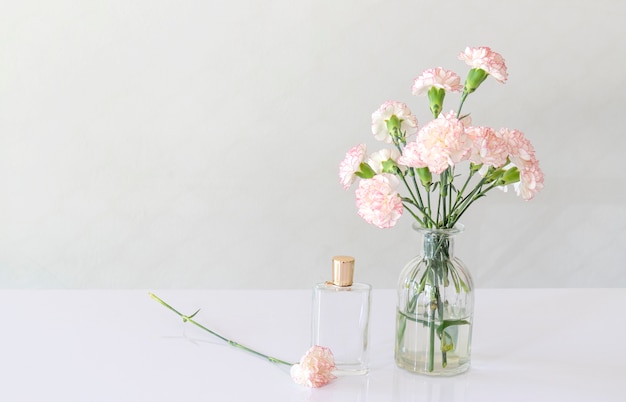 Bottiglia di profumo con vaso di fiori di garofano sul tavolo bianco.