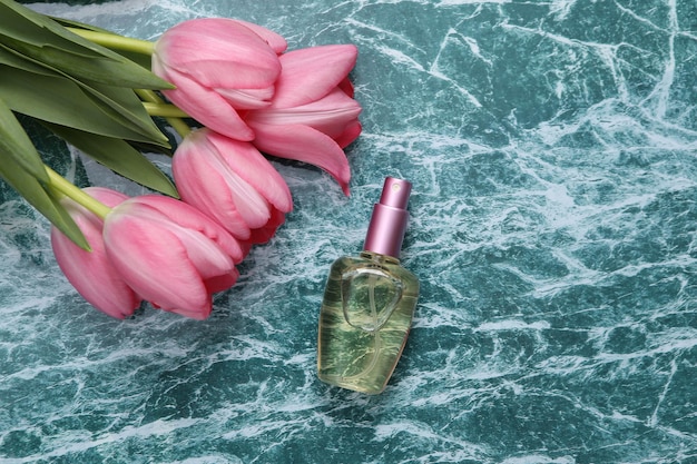 Bottiglia di profumo e tulipani rosa su superficie di marmo blu Concetto di bellezza romantica