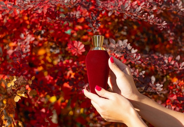 Bottiglia di profumo rossa in mano femminile che presenta una bottiglia di profumo che presenta un prodotto di bellezza