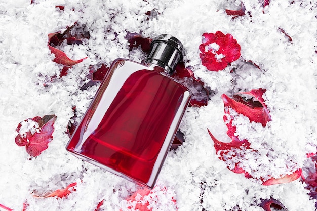 Bottiglia di profumo su foglie rosse coperte da sfondo di neve. Mockup di progettazione di imballaggi. Identità del marchio