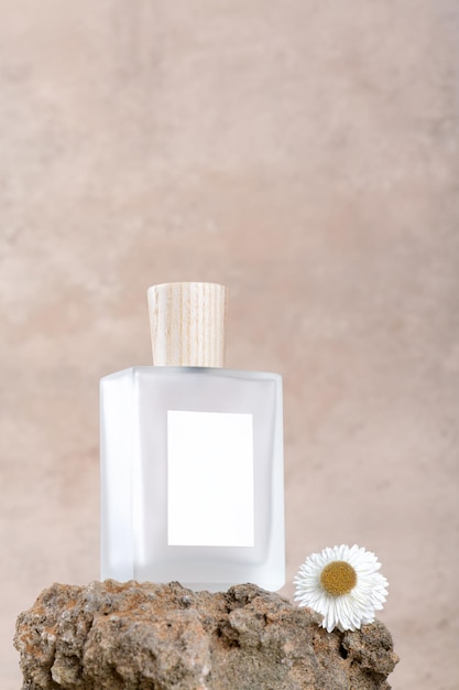 Bottiglia di profumo trasparente con etichette bianche su podio in pietra su fondo in terracotta beige con fiore secco