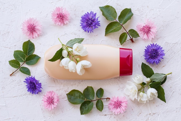 Bottiglia di shampoo con fiori di gelsomino e foglie verdi su sfondo bianco. Vista dall'alto.