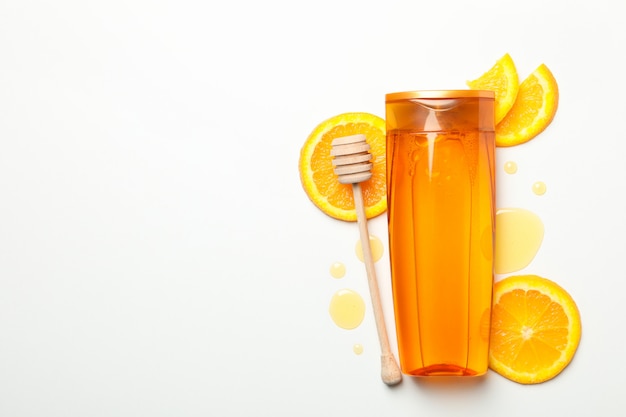 Bottiglia di shampoo, fette d'arancia e mestolo su sfondo bianco. Cosmetici naturali