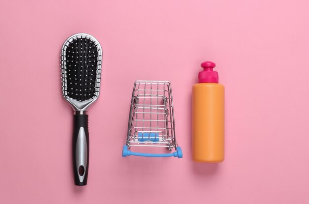 Bottiglia di shampoo, spazzola per capelli con mini carrello del supermercato su pastello rosa