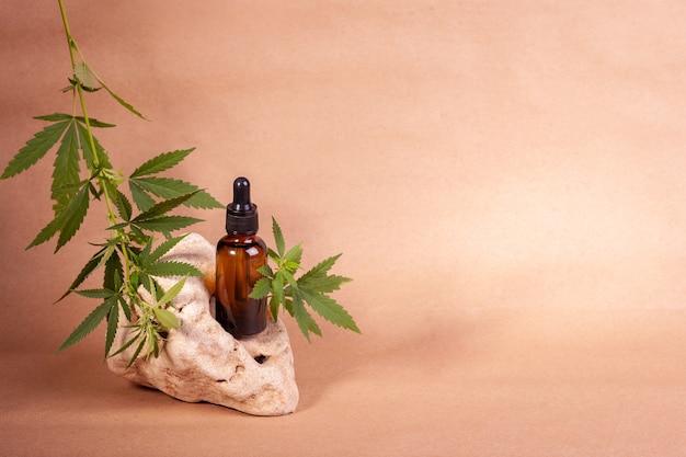 Bottiglia di siero con ramo di cannabis su pietra naturale su sfondo di carta artigianale.