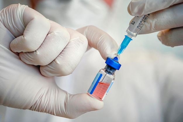 Bottiglia di vaccino ravvicinato nella mano di un medico con guanti bianchi su sfondo blu.