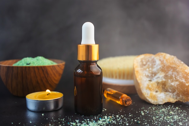 Bottiglia di vetro con pipetta, candela, piccola bottiglia di olio essenziale, pennello naturale e pietra decorativa sullo spazio buio Vapore - nell'aria Il concetto di procedure cosmetiche in bagno, bagno turco, sauna