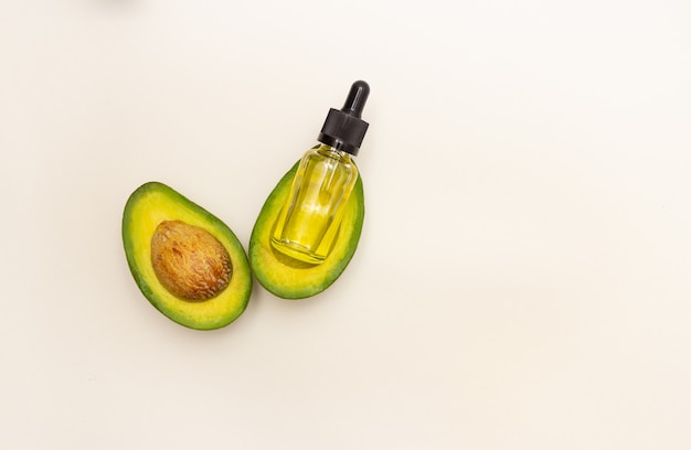 Bottiglia di vetro con pipetta e olio di avocado e frutto di avocado su sfondo chiaro, vista dall'alto, spazio libero per il testo