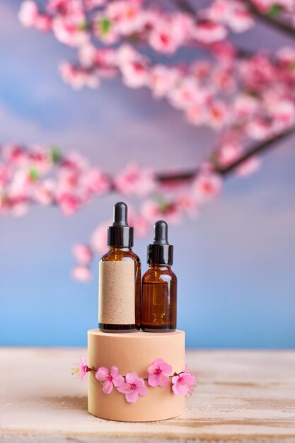 Bottiglia di vetro con pipetta e siero su un podio e rami di fiori di ciliegio