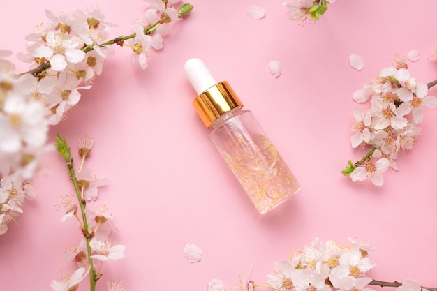 Bottiglia di vetro con siero d'olio su sfondo rosa con ciliegia in fiore Minimalismo piatto Strumenti cosmetici