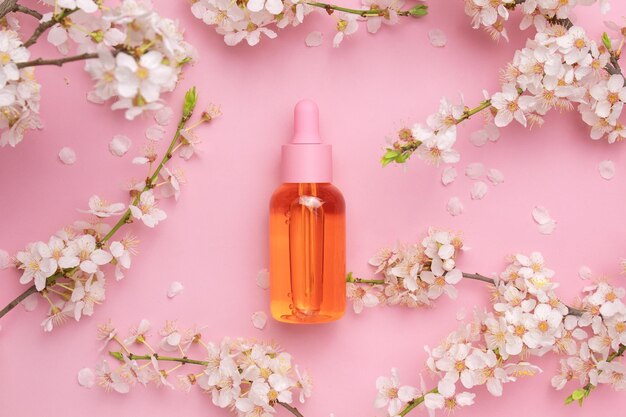 Bottiglia di vetro con siero d'olio su sfondo rosa con ciliegia in fiore Minimalismo piatto Strumenti cosmetici