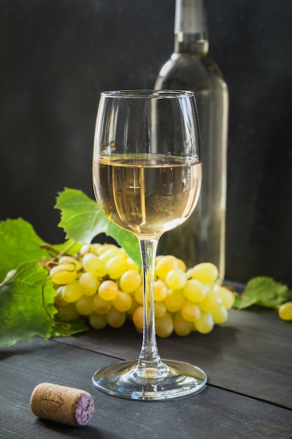 Bottiglia di vino bianco con bicchiere di vino, uva matura sul tavolo di legno nero.