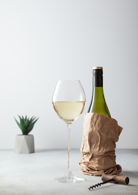 Bottiglia di vino bianco in sacchetto di carta con apritore e bicchiere di vino su sfondo chiaro