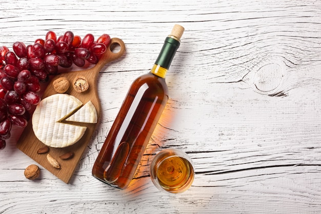 Bottiglia di vino bianco, uva, formaggio e bicchiere di vino sul bordo di legno bianco