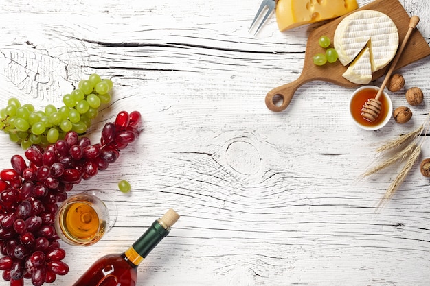 Bottiglia di vino bianco, uva, miele, formaggio e bicchiere di vino sul bordo di legno bianco