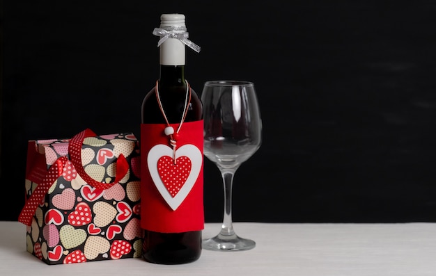 Bottiglia di vino, borsa della spesa, scatola bianca e cuore rosso di San Valentino sul nero