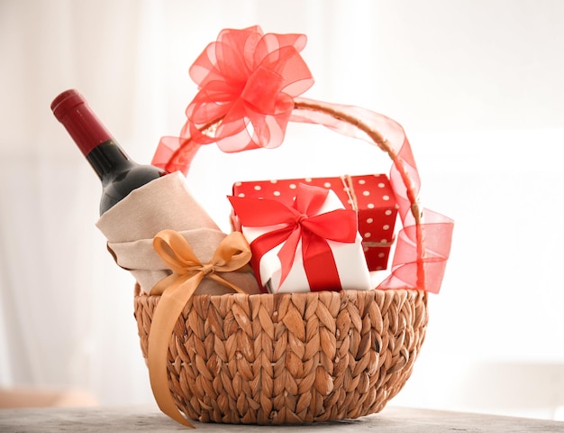 Bottiglia di vino con scatole regalo in cesto di vimini su sfondo chiaro