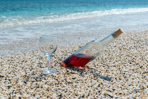 Bottiglia di vino rosso con bicchiere di vino sulla spiaggia durante la giornata di sole estivo