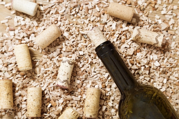 Bottiglia di vino rosso con tappi di sughero sul vecchio tavolo di legno con segatura sparsi.