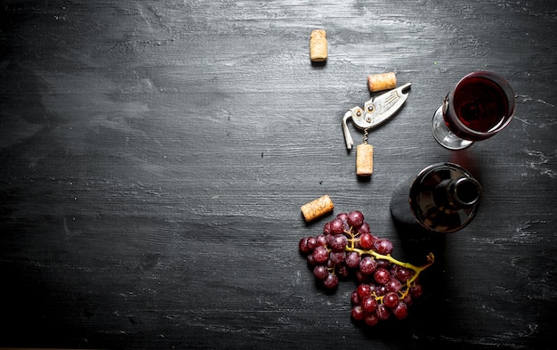 Bottiglia di vino rosso con un cavatappi sulla tavola di legno nera.