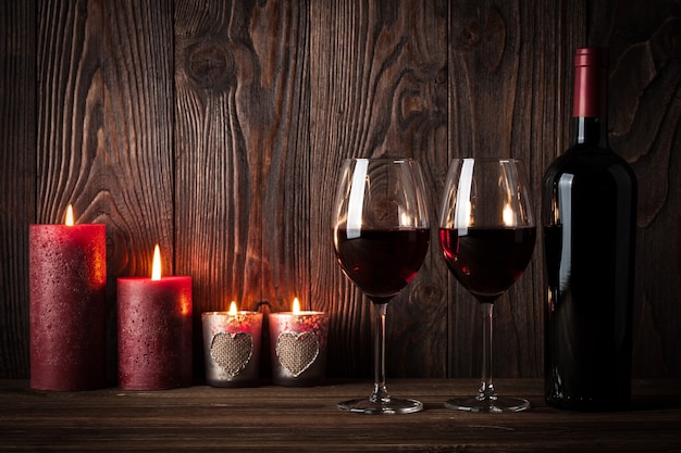 Bottiglia di vino rosso, due bicchieri di vino e candele sullo sfondo di legno scuro