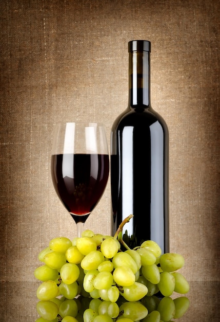 Bottiglia di vino rosso e uva su una tela di fondo