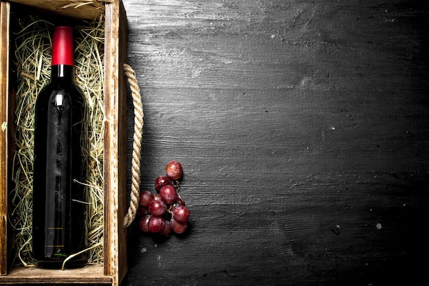 bottiglia di vino rosso in una vecchia scatola con un ramo d'uva. Sulla lavagna nera.