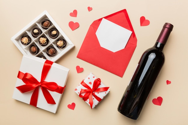 Bottiglia di vino rosso su sfondo colorato per San Valentino con confezione regalo, busta e cioccolato. A forma di cuore con confezione regalo di cioccolatini vista dall'alto con spazio per la copia.
