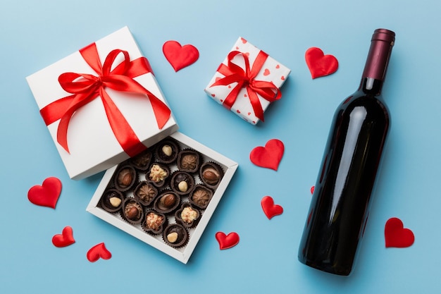 Bottiglia di vino rosso su sfondo colorato per San Valentino con regalo e cioccolato A forma di cuore con confezione regalo di cioccolatini vista dall'alto con spazio per la copia