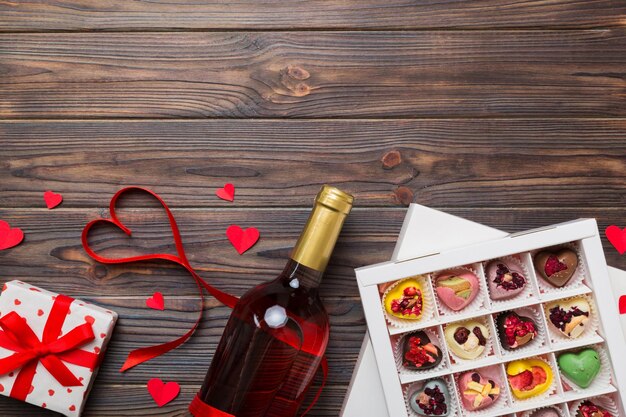 Bottiglia di vino rosso su sfondo colorato per San Valentino con regalo e cioccolato a forma di cuore con scatola regalo di cioccolatini vista superiore con spazio di copia