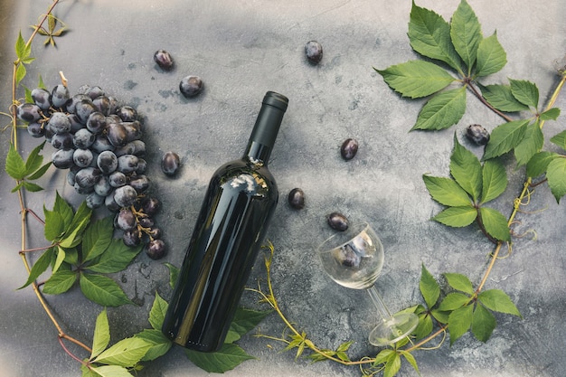 Bottiglia di vino rosso, vite verde, bicchiere di vino e uva matura su sfondo vintage tavolo in pietra scura. Copia spazio vista dall'alto per il testo. Enoteca wine bar cantina o concetto di degustazione di vini.