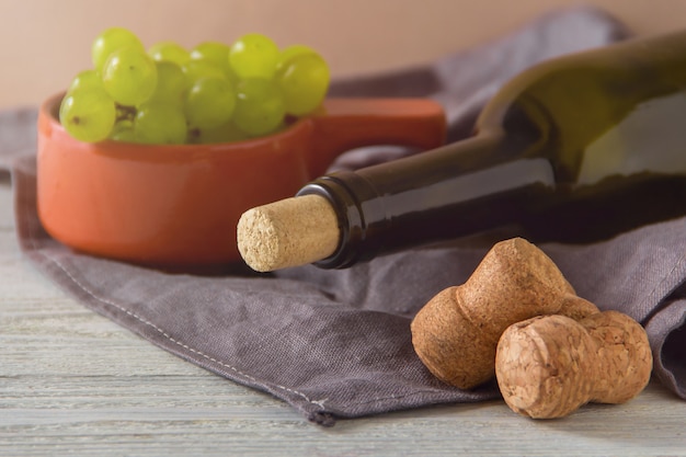 Bottiglia di vino, tappi di sughero, uva sul piatto sul tavolo.