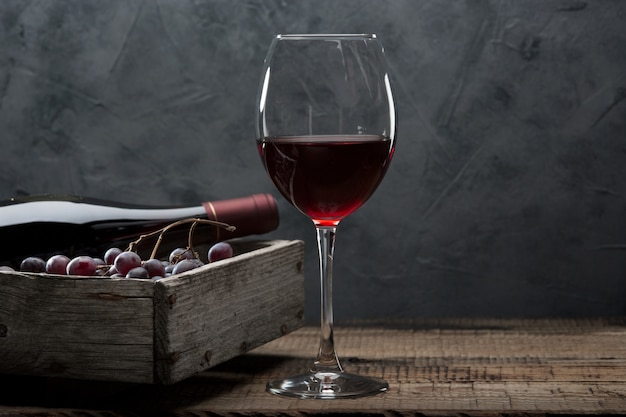 bottiglia di vino, un bicchiere, un grappolo d'uva e foglie di vite su un vecchio tavolo di legno.