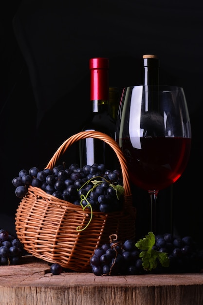 Bottiglia di vino, vino in vetro e cesto con uva