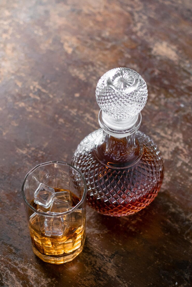 Bottiglia di whisky e bicchiere di whisky con ghiaccio su sfondo nero.