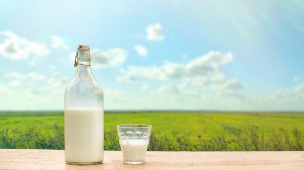 Bottiglia e bicchiere con latte fresco su uno sfondo di prato verde e cielo blu. Copia spazio. Banner largo